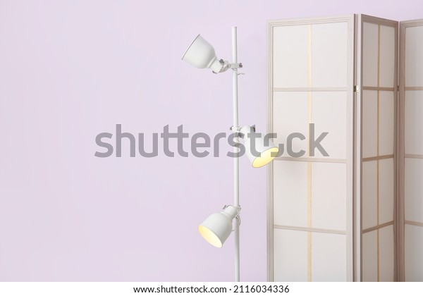 Stylish\
folding screen and lamp on light wall\
background
