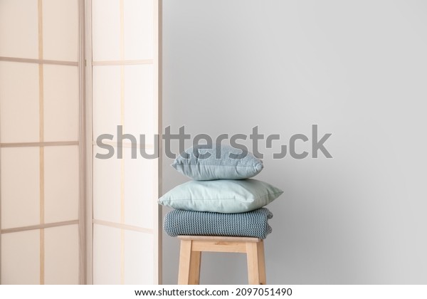 Stylish folding screen and pillows on stool\
near wall background