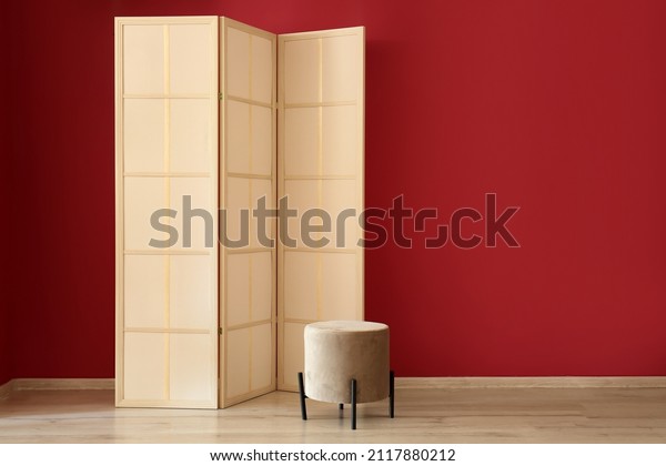 Stylish folding\
screen and pouf near red\
wall