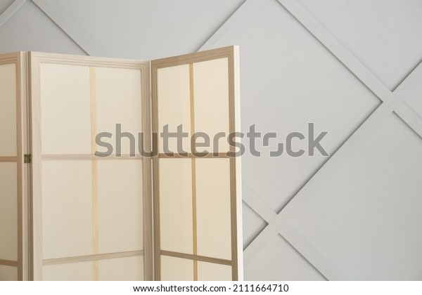 Stylish folding screen in room interior on\
wall background