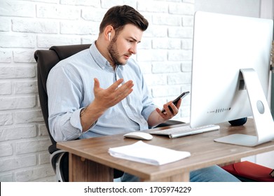 Stylish Formal Man Talks In Surprise On A Video Call Using A Phone And Airpods During A Workflow In The Office