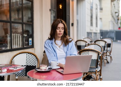 Stylish Freelancer Using Laptop Near Coffee And Dessert On Cafe Terrace In Paris