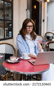 Stylish Freelancer Using Laptop Near Dessert And Coffee In Outdoor Cafe In Paris