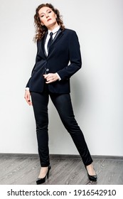 A Stylish Full-length Woman Poses In A Black Tuxedo With Luxurious Hair On A White Background In The Photo Studio Of Fashion Cover Magazine.