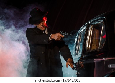 Stylish Gangster Holding Gun Near Retro Car On Black With Smoke 