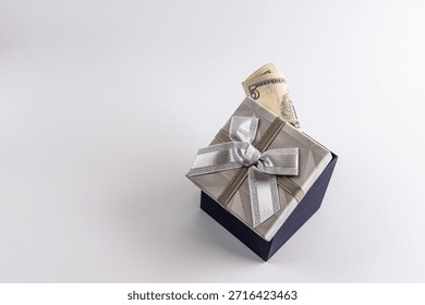 A stylish gift box features a silver ribbon and bow, with cash peeking from the top. Perfect for themes of gift-giving, luxury, celebration, and surprise in a premium setting.