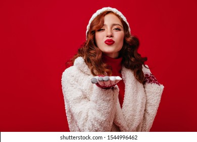 Stylish Girl Of 20 Years Old In High Spirits Is Flirting And Blowing Air Kiss. Photo Of Lady In Comfortable Warm Clothes And Bright Coat