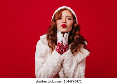 Stylish Girl Of 20 Years Old In High Spirits Is Flirting And Blowing Air Kiss. Photo Of Lady In Comfortable Warm Clothes And Bright Coat