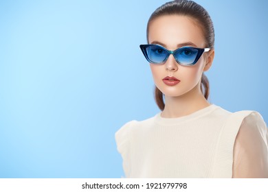 Stylish Girl. Beautiful Summer Girl Posing In Elegant White Clothes And Sunglasses On A Light Blue Background. Summer Fashion And Optics. Copy Space.