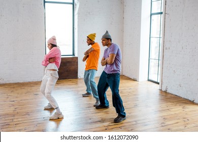 stylish girl with crossed arms breakdancing with handsome multicultural men in hats