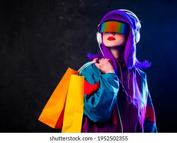 Stilvolles Mädchen in Cyber-Punk-Brillen und 80er-Tracksuit mit Einkaufstüten und Kopfhörern auf dunklem Hintergrund