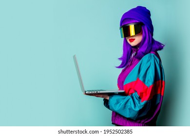 Stylish Girl In Cyber Punk Glasses And 80s Tracksuit Hold Laptop Computer On Blue Background