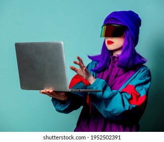 Stylish Girl In Cyber Punk Glasses And 80s Tracksuit Hold Laptop Computer On Blue Background