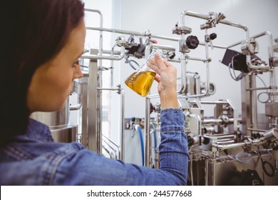 Stylish girl in denim jacket holding beaker of beer in the factory