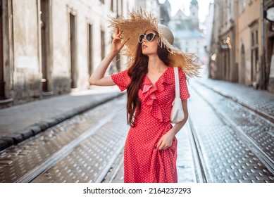 Stylish girl in summer outfit: straw hat, sunglasses, red dress, white bag walk on old city streets - Powered by Shutterstock