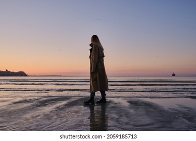 Stylish girl walks at sunset along the beach of the sea or ocean on a cool day. Travel concept. Walk on the sea or ocean. Girl in travel. Amazing scenic outdoors view. Beautiful sunset on the seashore - Powered by Shutterstock
