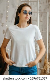 Stylish girl wearing white t-shirt and sunglasses posing in studio