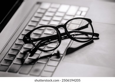 Stylish glasses rest on a laptop keyboard, providing essential eye protection during extended computer use. Ideal for reducing digital eye strain during long hours of screen time. - Powered by Shutterstock