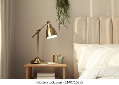 Elegante lámpara dorada y papelería en una mesa de noche de madera en el dormitorio. Elemento de interior