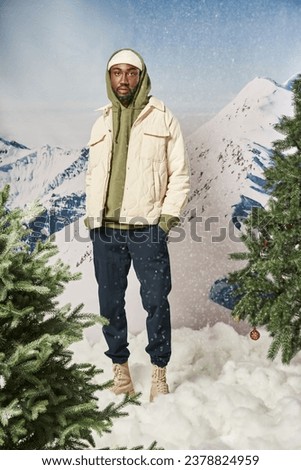 stylish good looking man posing under snowfall with hands in pockets looking at camera, winter