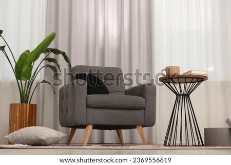 Stylish gray armchair and small table in living room. Interior design