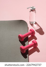 Stylish gray and pink fitness training and gym concept. Perspective view of gray sport mat, water bottle and pink dumbbells on pink background. Set for pilates, fitness with copy space. Vetical - Shutterstock ID 2267942737