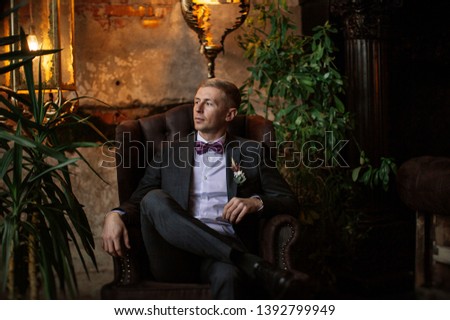 stylish groom in a gray suit posing in a vintage room