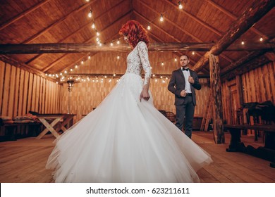 Stylish Groom And Happy Bride Dancing Under Retro Bulbs Lights In Wooden Barn. Rustic Wedding Concept, Space For Text. Newlyweds Couple Embracing, Sensual Romantic Moment