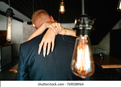 Stylish Groom And Happy Bride Kissing Under Retro Bulbs Lights In Wooden Barn. Rustic Wedding Concept, Space For Text. Newlyweds Couple Embracing, Sensual Romantic Moment