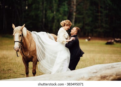 stylish  groom helps beautiful bride to get off brown horse in the autumn park