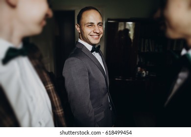 Stylish Groom Laughing And Having Fun With Groomsmen While Getting Ready In The Morning For Wedding Ceremony. Luxury Man In Suit With His Friends Smiling In Room. Space For Text.