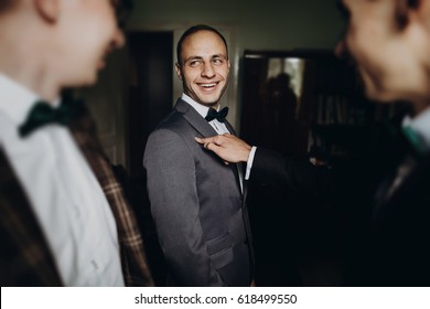 Stylish Groom Laughing And Having Fun With Groomsmen While Getting Ready In The Morning For Wedding Ceremony. Luxury Man In Suit With His Friends Smiling In Room. Space For Text.