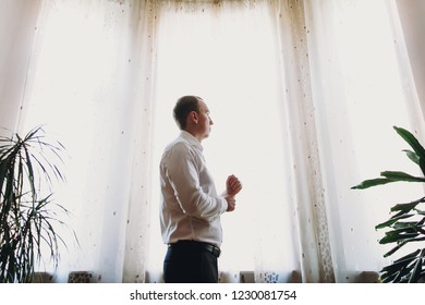 Stylish groom putting on white shirt, getting ready in the morning near window in soft light, before wedding ceremony - Shutterstock ID 1230081754