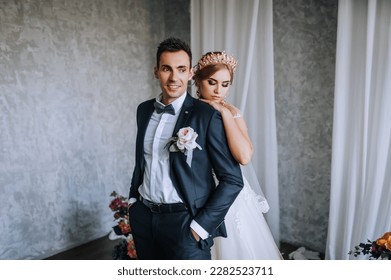 Stylish groom in a suit and a beautiful blonde model bride with a crown, diadem, in a white dress are hugging in the studio, interior. Wedding photography, portrait of happy, smiling newlyweds. - Powered by Shutterstock