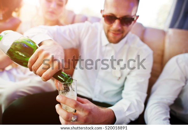 Stylish\
groomsman or best man of groom and bridesmaids  inside limousine at\
wedding party pours champagne in\
glasses.