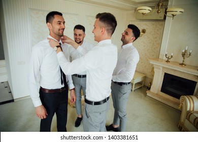 stylish groomsmen helping happy groom getting ready in the morning for wedding ceremony. luxury man in suit in room. space for text. wedding day