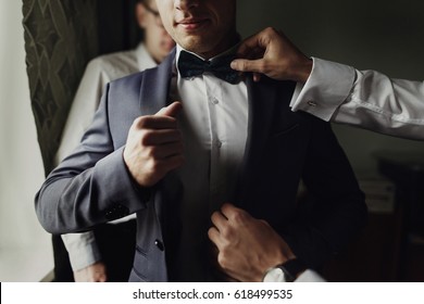 stylish groomsmen helping happy groom getting ready in the morning for wedding ceremony. luxury man in suit in room. space for text. wedding day. - Powered by Shutterstock