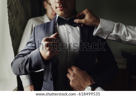 stylish groomsmen helping happy groom getting ready in the morning for wedding ceremony. luxury man in suit in room. space for text. wedding day.