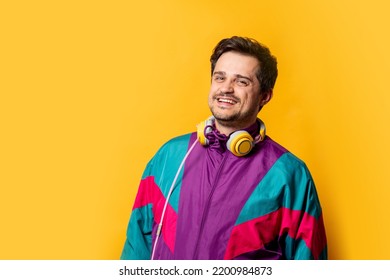 Stylish guy in 80s sport suit with headphones on yellow background