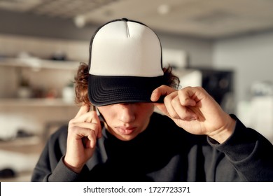 Stylish guy looking down while posing in custom apparel, black baseball cap and sweatshirt. Young man working at custom T-shirt, clothing printing company. Horizontal shot
