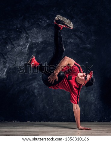 Stylish guy performs breakdance acrobatic elements. Studio photo against a dark textured wall