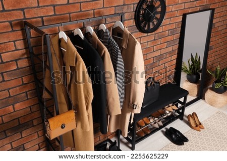 Stylish hallway with coat rack and shoe storage bench near brick wall. Interior design