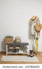 Stylish Hallway Interior With Coat Rack And Shoe Storage Bench Near White Brick Wall