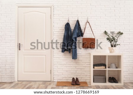 Stylish hallway interior with door, comfortable furniture and clothes on brick wall