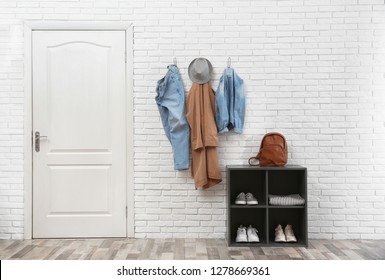 Stylish Hallway Interior With Door, Shoe Rack And Clothes Hanging On Brick Wall