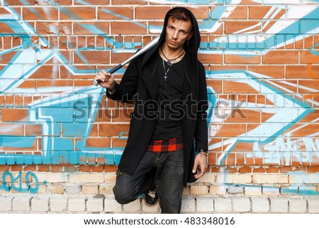 Stylish handsome man with a bat is posing near brick wall with graffiti.