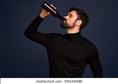 Stylish Handsome Man In Trendy Black Sweater Drinking From Beer Bottle Over Pacific Blue Background.