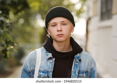 Stylish handsome teen boy 16-17 year old wearing denim jacket and knit hat over city background close up. Teenagerhood. 