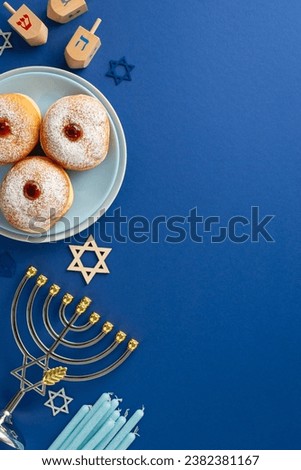 Stylish Hanukkah table arrangement. Top view vertical image of traditional Jewish meal - sufganiyot, Star of David, menorah, and dreidel game on blue background, space for text or advertising