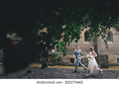 Stylish happy bride and groom running and smiling on background of church under tree leaves. Provence wedding. Beautiful emotional wedding couple in european city. - Powered by Shutterstock